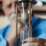 Elderly man holding a metal hourglass, focusing on the sand timer.